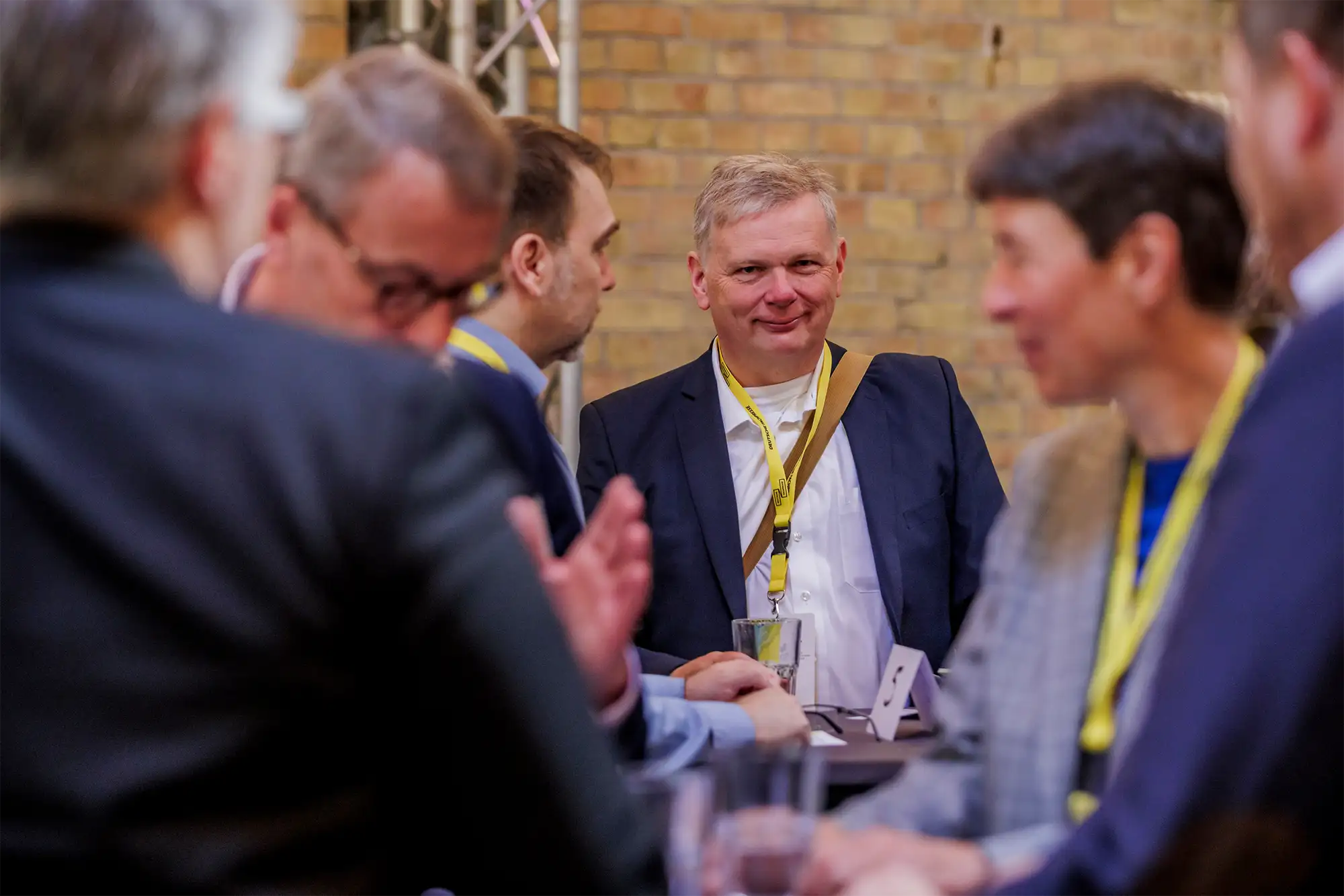 Personengruppe bei bei den B2B Media Days, ein lächelnder Mann steht im Fokus, während die übrigen Teilnehmer miteinander sprechen