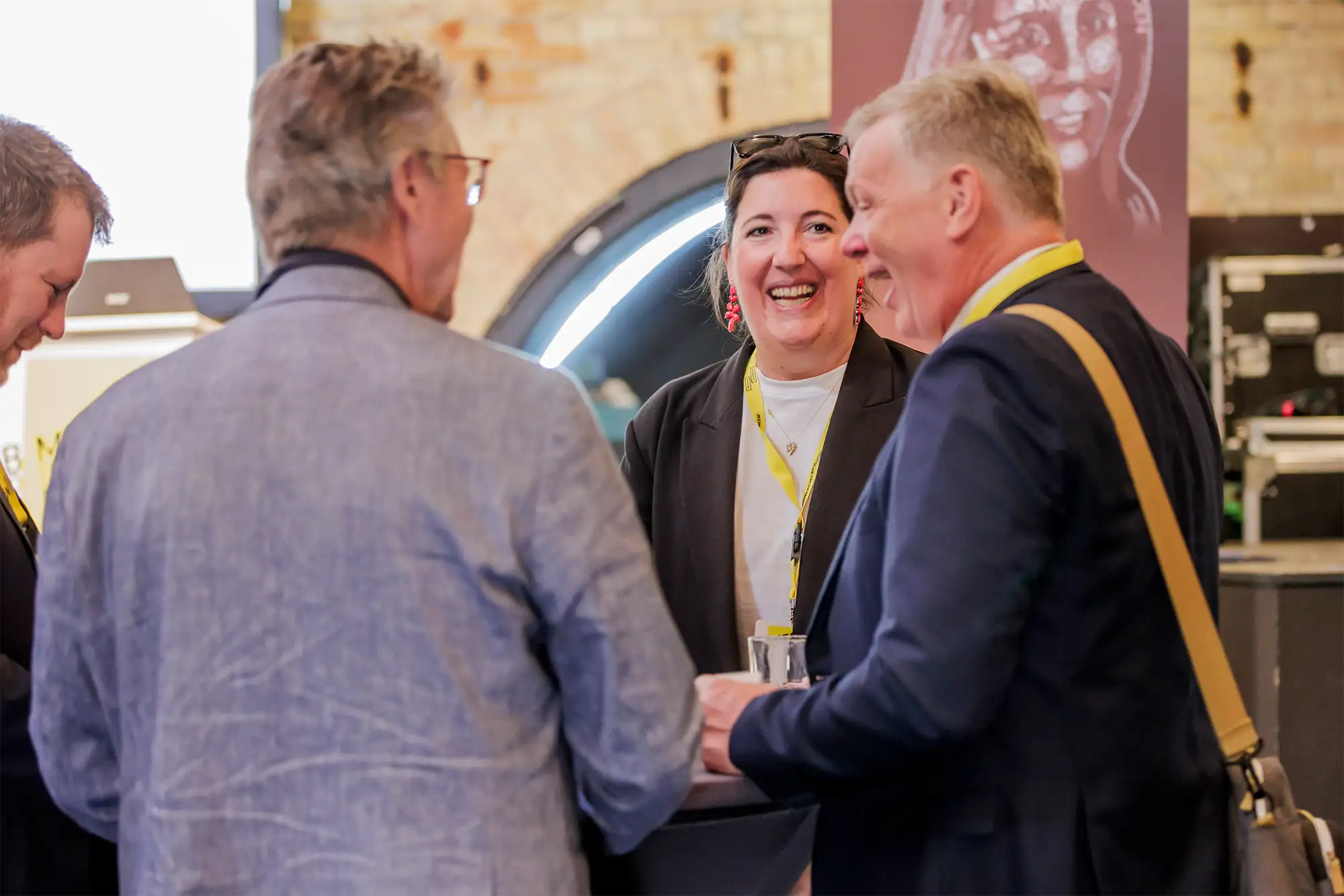 Lachende Frau mit gelbem Lanyard in einer Gesprächsrunde bei den B2B Media Days, flankiert von zwei männlichen Teilnehmern in Anzügen.