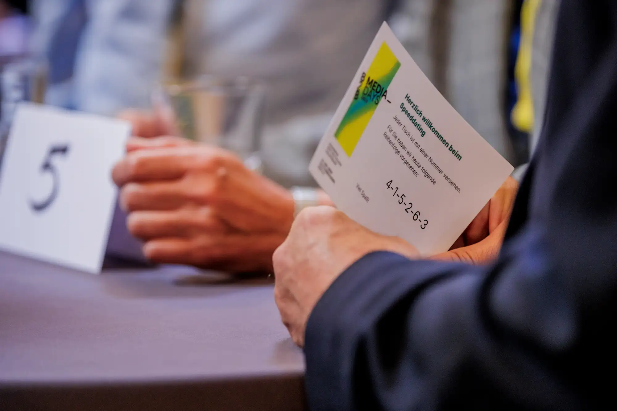 Nahaufnahme eines Teilnehmers, der eine Karte mit Informationen für ein Speeddating-Event bei den B2B Media Days 2023 hält.
